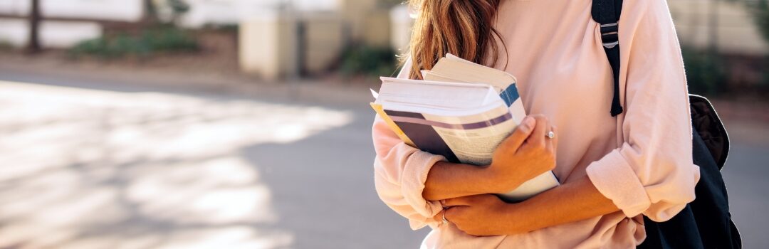 close up of a student wearing a pink shirt with long hair holding textbooks